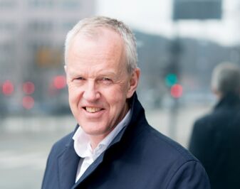 Mann i blå jakke smiler til kamera. Foto