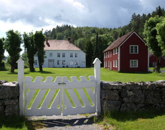 Hvit port inn til to trehus omgitt av skog