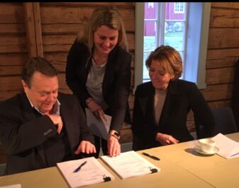 Tre mennesker ved et bord som signerer dokumenter